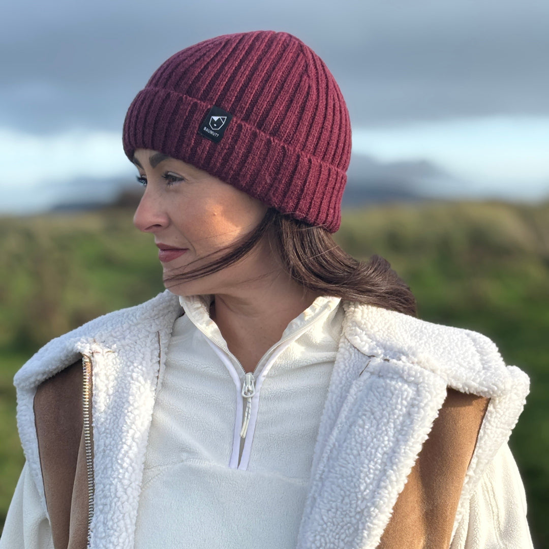 A burgundy red BAUMUTT fisherman beanie hat with a snug fit, designed for men and women. side view on female model